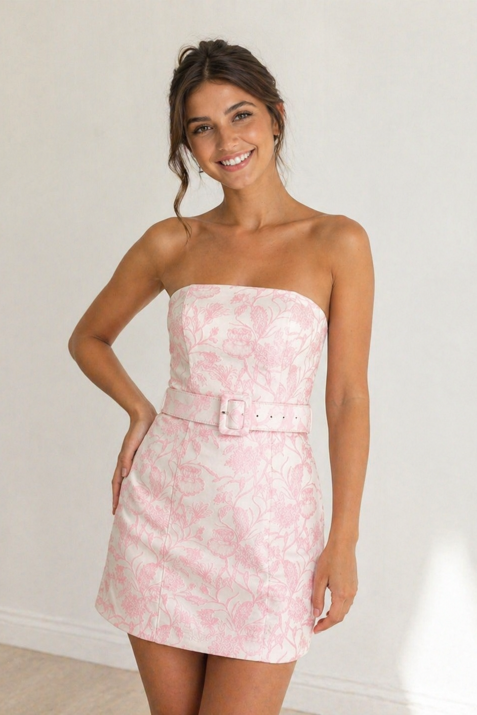 Woman wearing a pink strapless dress with a belt against a white background