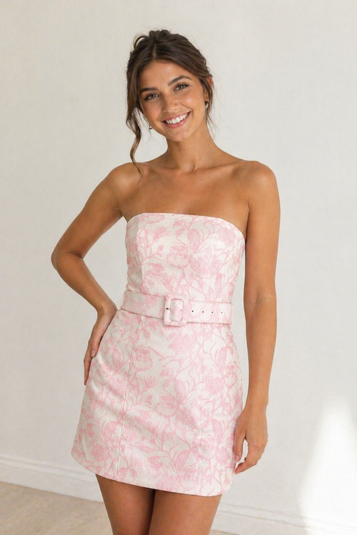 Woman wearing a pink strapless dress with a belt against a white background